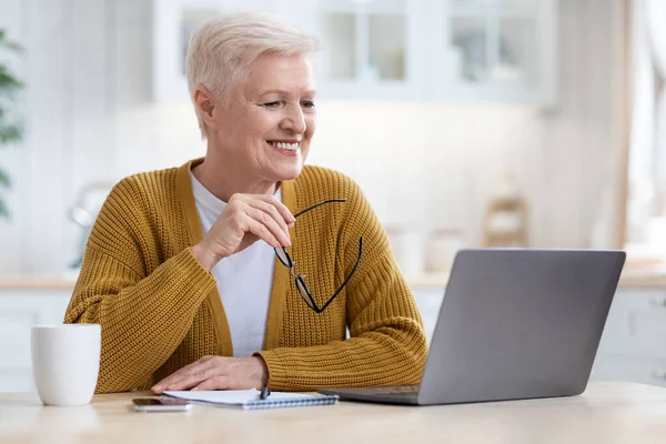 Seniorin blickt auf Laptop-Bildschirm und lächelt — Stockfoto