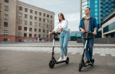 Genç adam ve bayan elektrikli scooterla geziyorlar.