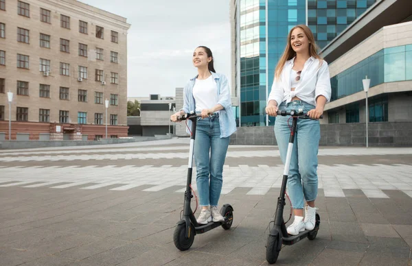 Ženy přátelé na koni motorizované koloběžky ve městě — Stock fotografie