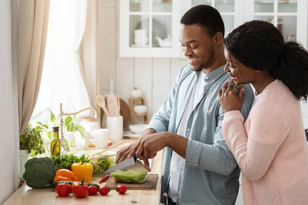 Cocinando juntos. Retrato de feliz pareja negra afectuosa preparando el almuerzo en la cocina — Foto de Stock
