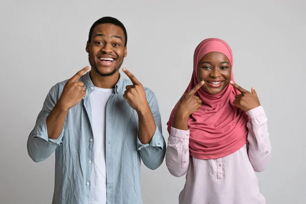Glimlachende zwarte man en vrouw wijzen naar hun witte tanden — Stockfoto