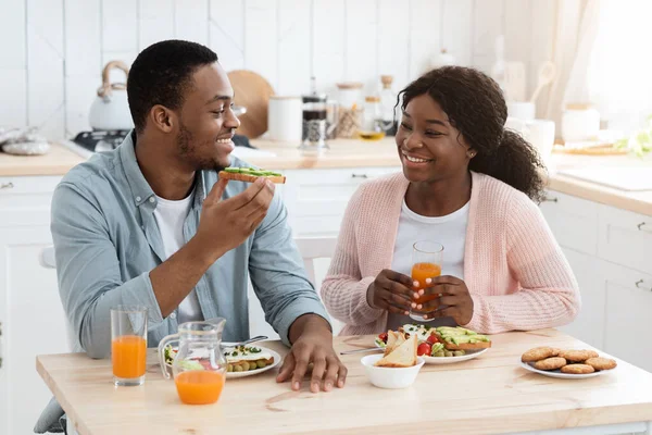 Alegre afroamericano cónyuges comiendo comida en cocina y tener charla — Foto de Stock