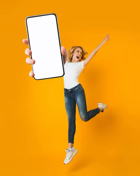 Donna bionda emotiva che salta e urla, impazzisce, mostra smartphone con spazio per la nuova app mobile sullo schermo — Foto Stock