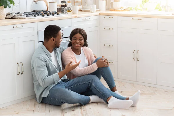 Heureux homme et femme noirs assis sur le sol dans la cuisine et bavarder — Photo