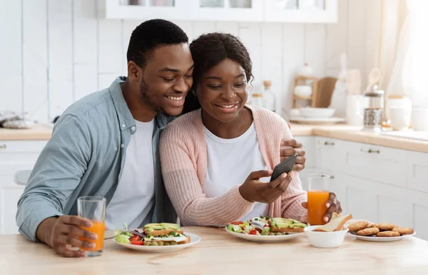 Cónyuges afroamericanos románticos revisando la nueva aplicación en el teléfono inteligente durante el desayuno — Foto de Stock