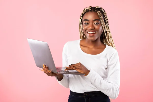 Sonriente joven dama negra sosteniendo y utilizando el ordenador portátil en el estudio — Foto de Stock