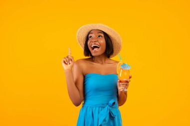 Lezzetli tropikal kokteyli olan Milenyum siyahi kadın çığlık atıyor ve turuncu stüdyo arka planına işaret ediyor.