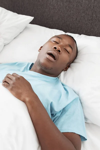 Tired man sleeping on bed with snore face at cozy home