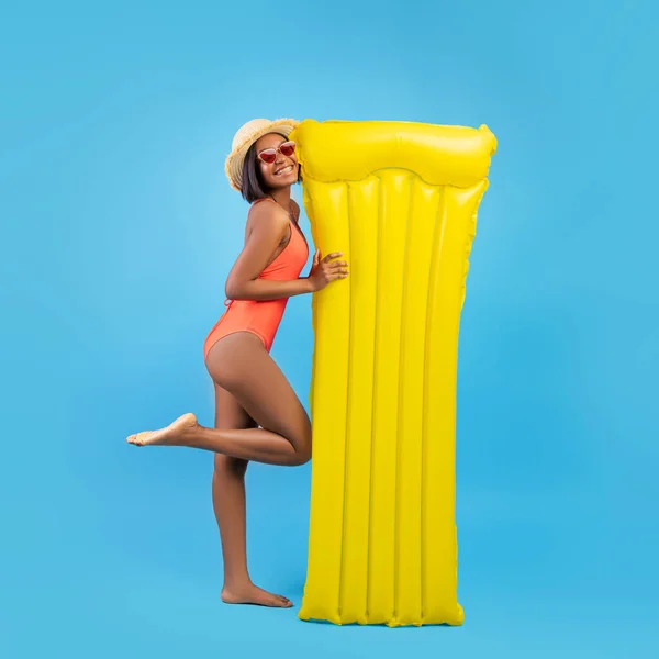 Az úszás jó móka. Vidám fekete nő fürdőruhában megy medence sárga felfújható lilo felett kék stúdió háttér — Stock Fotó