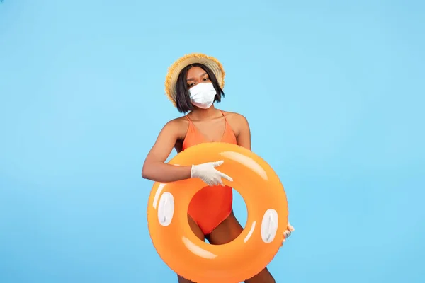 Vacanze estive durante l'isolamento Covid. Donna nera in costume da bagno, maschera facciale e guanti di gomma con anello gonfiabile — Foto Stock