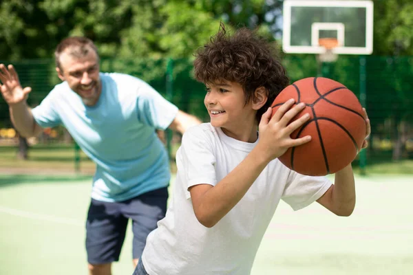 Sportive dad teaching his son how to play basketball outside — Stock Photo, Image