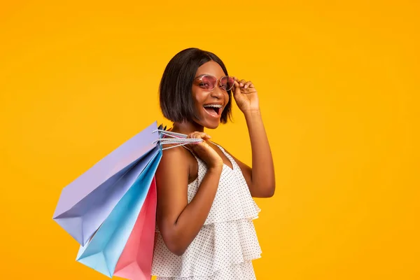 Vendas sazonais. Mulher negra bonita com sacos de compras gritando WOW e olhando para a câmera no fundo laranja — Fotografia de Stock