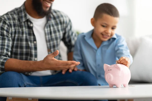 Pai e filho colocando poupanças pessoais em Piggybank dentro de casa, cortado — Fotografia de Stock