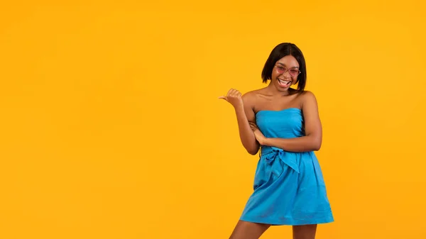 Красивая афроамериканка в платьях и солнцезащитных очках, указывающая на пустое пространство на оранжевом фоне, дизайн баннера — стоковое фото