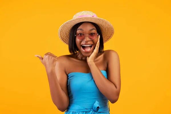 Portrait de jeune femme noire excitée en tenue tendance criant WOW et pointant de côté sur fond orange — Photo