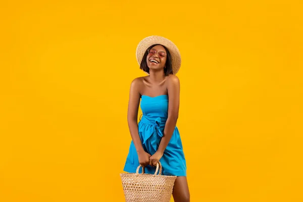 Beautiful black woman in summer outfit holding beach bag, laughing and enjoying her vacation on orange background — Stock Photo, Image