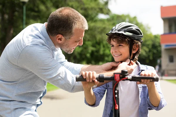 Smiling adult man putting safety helmet on his son — Stock Photo, Image