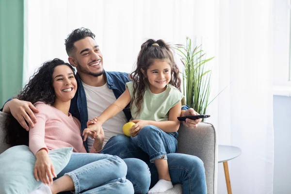 Fin de semana familiar. Alegre árabe padres y poco hija viendo la televisión en casa — Foto de Stock