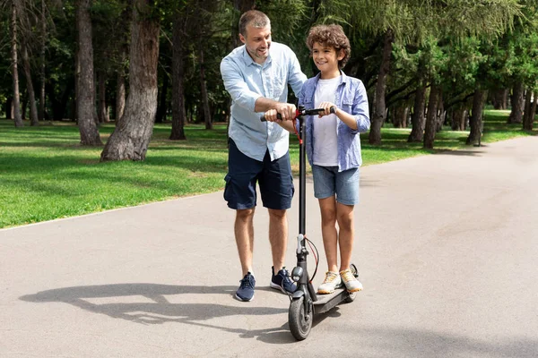 Chlapec se učí jezdit na e-scooter se svým dospělým otcem — Stock fotografie