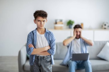 Nesiller boyu yanlış anlaşılma. Babası dizüstü bilgisayarla arka planda çalışırken ön planda duran saldırgan çocuk