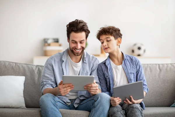 Σύγχρονες τεχνολογίες. Ο γιος και ο μπαμπάς παίζουν online βιντεοπαιχνίδια σε ψηφιακά tablet, ενώ κάθονται στον καναπέ στο σπίτι — Φωτογραφία Αρχείου