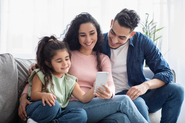 Sonriente familia de Oriente Medio con la pequeña hija usando Smartphone juntos en casa — Foto de Stock