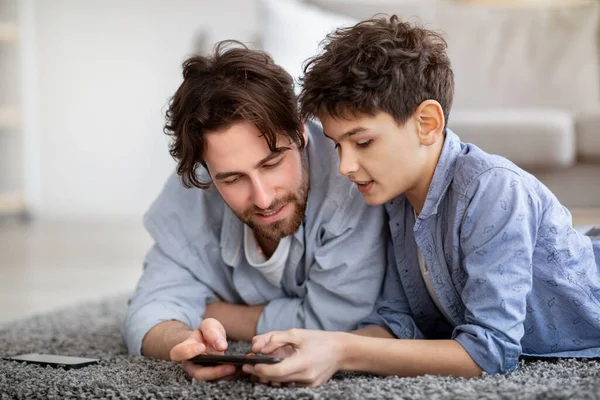 Far och son använder smartphone, titta på bilder eller pojke hjälpa pappa med spelet, tillbringa tid hemma — Stockfoto