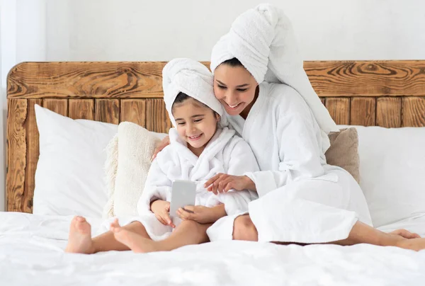 Bella madre e figlia in accappatoi utilizzando il telefono cellulare — Foto Stock