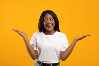 Kafası karışmış zenci kadın sarı stüdyo arka planında el kaldırıyor.