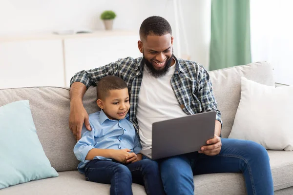 Nero papà e figlio guardando film su computer portatile a casa — Foto Stock