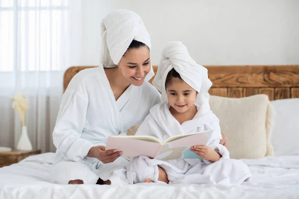 Alegre madre e hija en batas leyendo cuentos de hadas —  Fotos de Stock