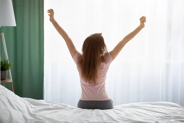 Vista posterior de la mujer joven estirándose en la cama después de despertarse en casa —  Fotos de Stock