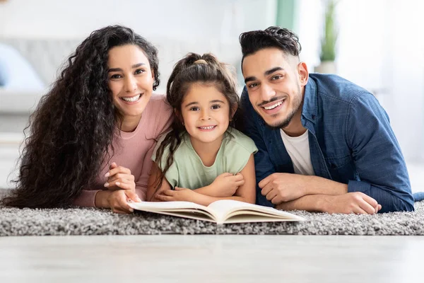 Passatempos e atividades familiares. Pais árabes felizes lendo o livro com a filha pequena — Fotografia de Stock