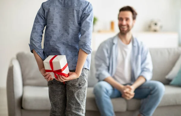 Garçon saluant son jeune père avec Fathers Day, cachant boîte cadeau derrière son dos, foyer sélectif — Photo