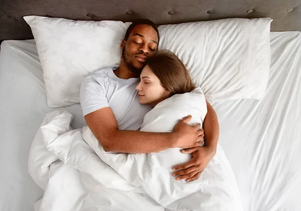 Sevecen, çok ırklı bir çiftin yatakta uyurken birbirlerine sarılışının üst görüntüsü. — Stok fotoğraf