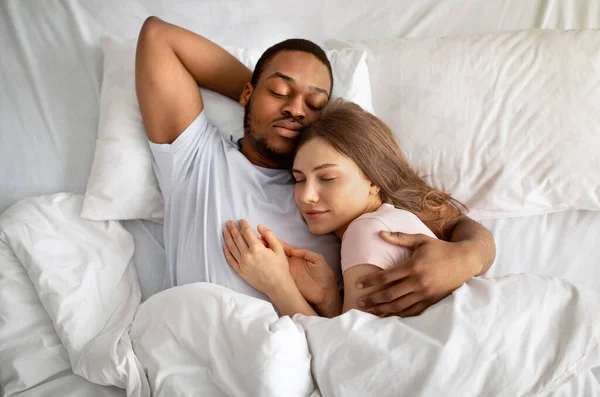 Affettuosa coppia interrazziale che dorme a letto e si abbraccia, vista dall'alto. Concetto di amore e relazioni — Foto Stock