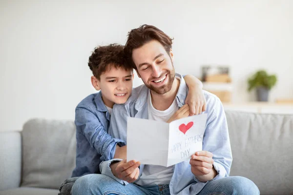 Concepto del día de los padres. Hijo felicitando a papá y dándole postal hecha a mano, tarjeta de lectura de papá y sonriendo — Foto de Stock