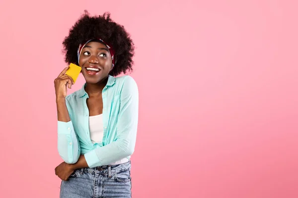 Alegre dama negra sosteniendo tarjeta de crédito mirando a un lado, fondo rosa —  Fotos de Stock