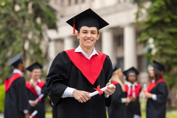 Schöner Kerl Student im Abschlusskostüm zeigt Diplom — Stockfoto
