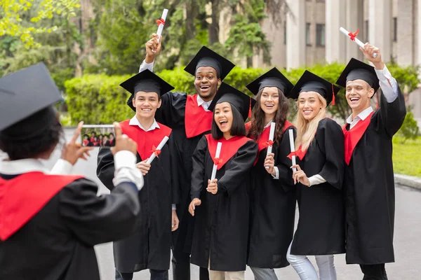 Emocionální multiraciální studenti mají promoční večírek, fotografování — Stock fotografie