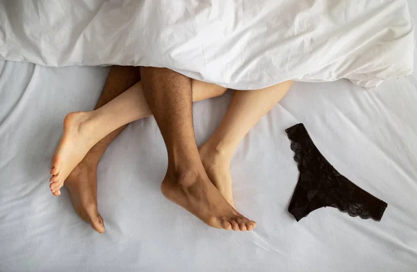 Top view of young multiracial couple making love on bed, cute panties lying nearby — Stock Photo, Image