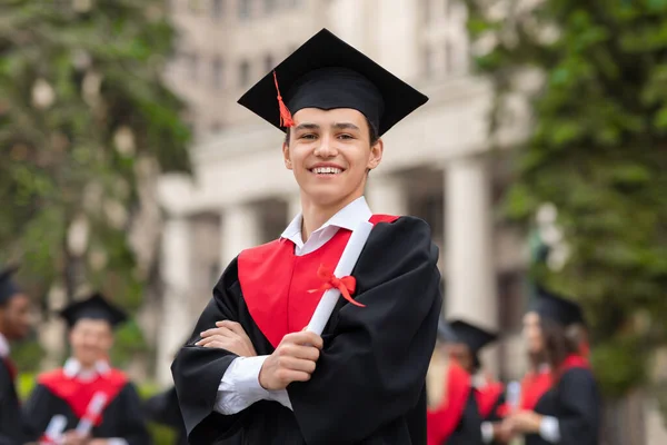 Happy young man student in graduation costume showing diploma