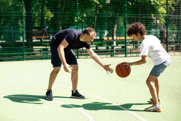 Αθλητικός άντρας που μαθαίνει στο αγόρι πώς να παίζει μπάσκετ έξω. — Φωτογραφία Αρχείου