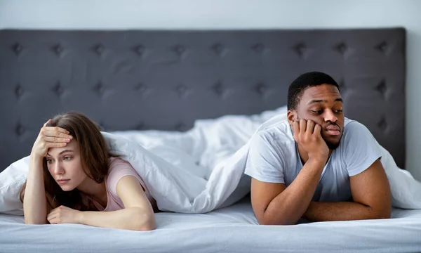 Csalódott fekete férfi és kaukázusi nő veszekednek, takaró alatt fekszenek az ágyon, nem nézik egymást. — Stock Fotó