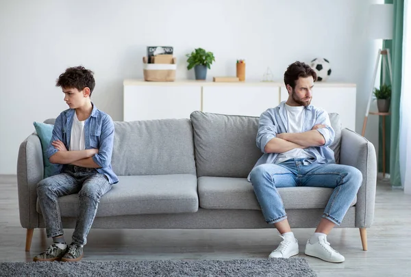 Las generaciones familiares entran en conflicto. Padre e hijo ofendidos sentados en diferentes lados del sofá, ignorándose después de discutir —  Fotos de Stock