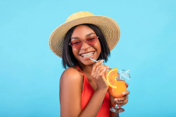 Retrato de mujer negra fresca en traje de baño, sombrero de paja y gafas de sol bebiendo cóctel de verano exótico sobre fondo azul —  Fotos de Stock