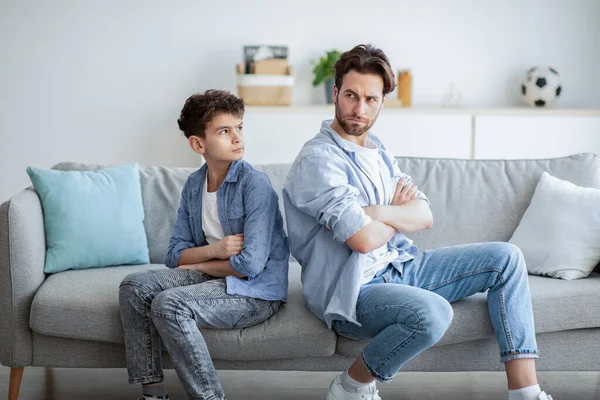 Οικογενειακή διαφωνία. Ο θυμωμένος πατέρας και ο γιος του κάθονται πλάτη με πλάτη στον καναπέ στο σπίτι μετά τον καυγά. — Φωτογραφία Αρχείου