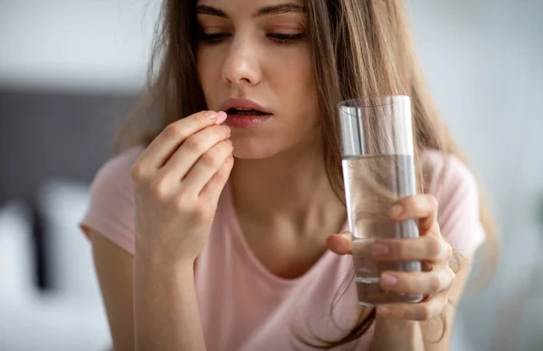 Jovem perturbada com copo de água tomando pílula, não se sentindo bem, usando drogas médicas em casa — Fotografia de Stock