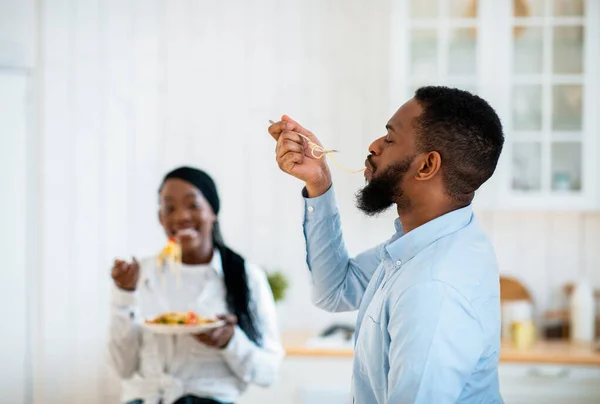 Deliciosa comida. Hambriento afroamericano hombre sorbiendo espaguetis largos en la cocina — Foto de Stock