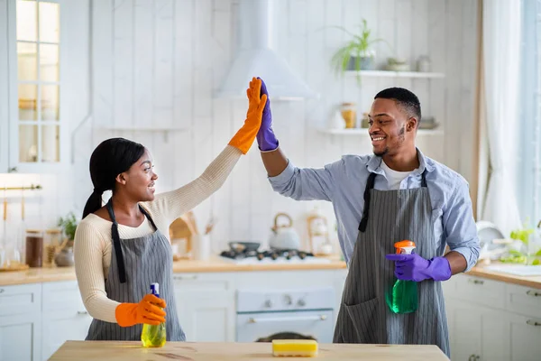 Młoda czarna para w gumowych rękawiczkach przybija sobie piątkę podczas prac domowych w kuchni — Zdjęcie stockowe